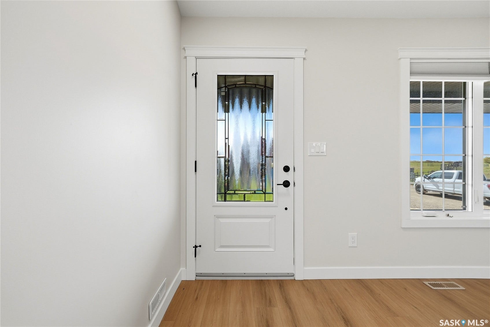 White interior walls, wood-finish flooring, white entry door with decorative glass inlay, white window trim, and a white framed window