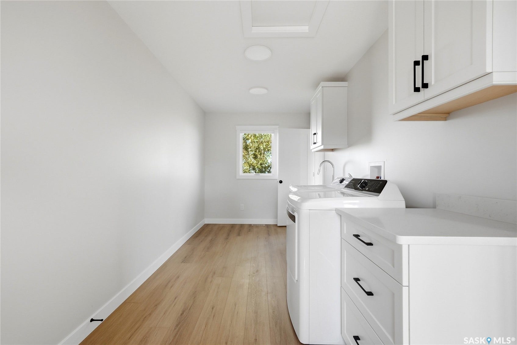 Laundry room featuring wood-finish flooring, white cabinetry with black hardware, and an integrated sink