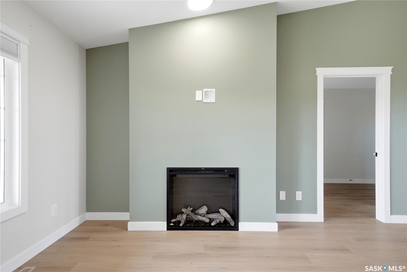 Electric fireplace, wood-finish flooring, vaulted ceiling, white trim, and a window with blinds