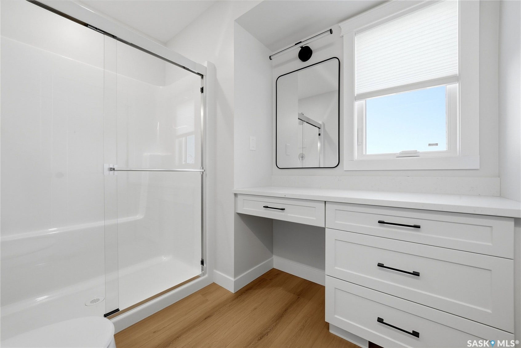 Walk-in shower with clear glass enclosure, white vanity with integrated drawers, quartz countertop, and wood-finish flooring