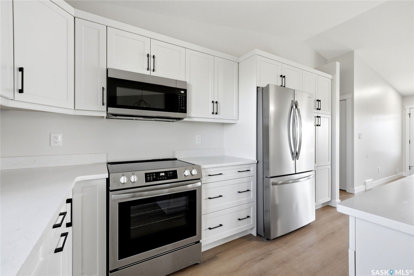 White cabinetry, stainless steel appliances, light-toned wood-finish flooring, white countertops, and black hardware