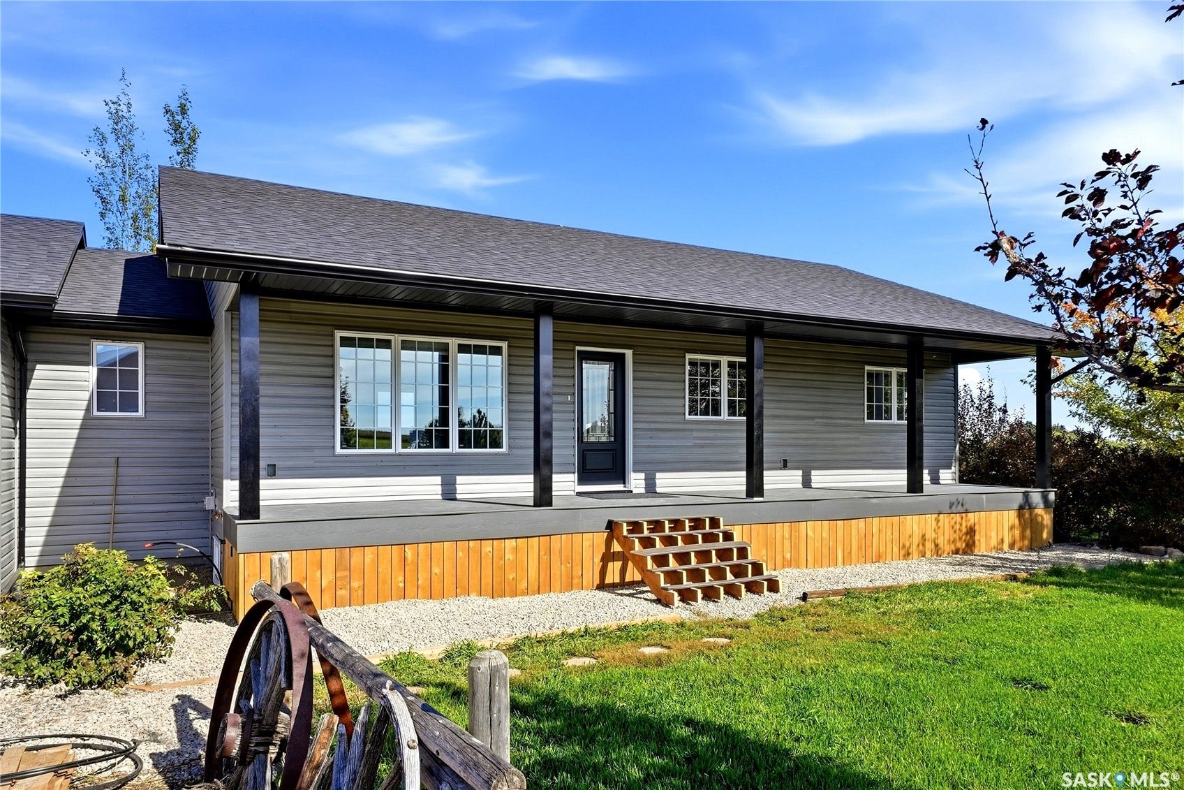 Covered front porch with dark support columns, gray siding, a dark roof, and a wood-finish porch base