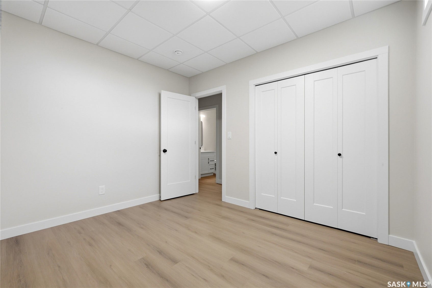 Light wood-finish flooring, white walls, white trim, bi-fold closet doors, and recessed ceiling panels