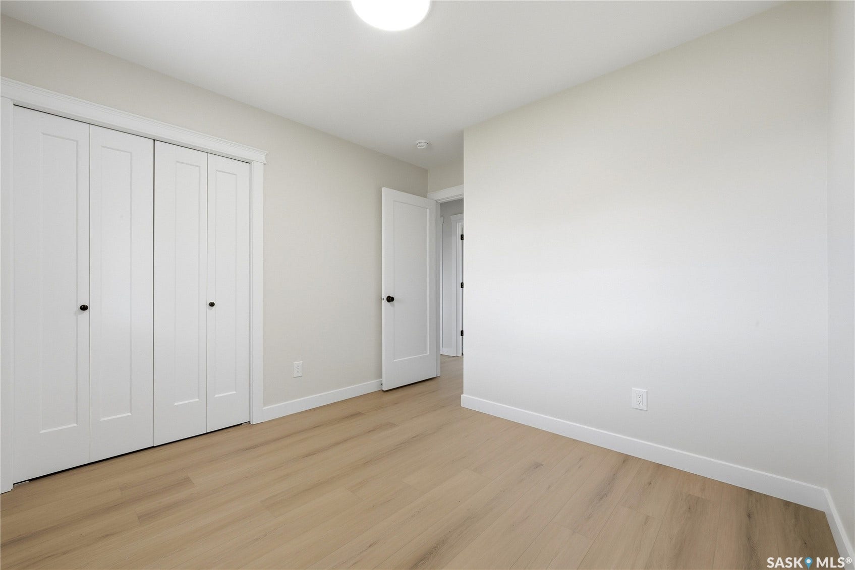 Light wood-finish flooring, white walls, white trim, and white bi-fold closet doors