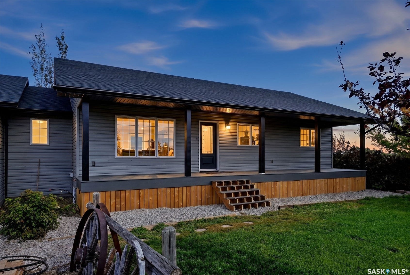 Property with gray horizontal siding, dark roof, expansive covered porch, and natural wood steps
