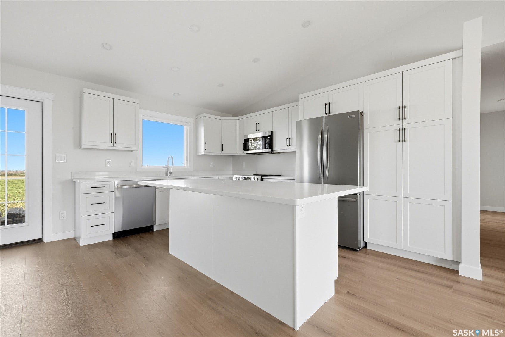 White shaker cabinetry with black hardware, stainless steel appliances, solid surface countertops, and wood-finish flooring
