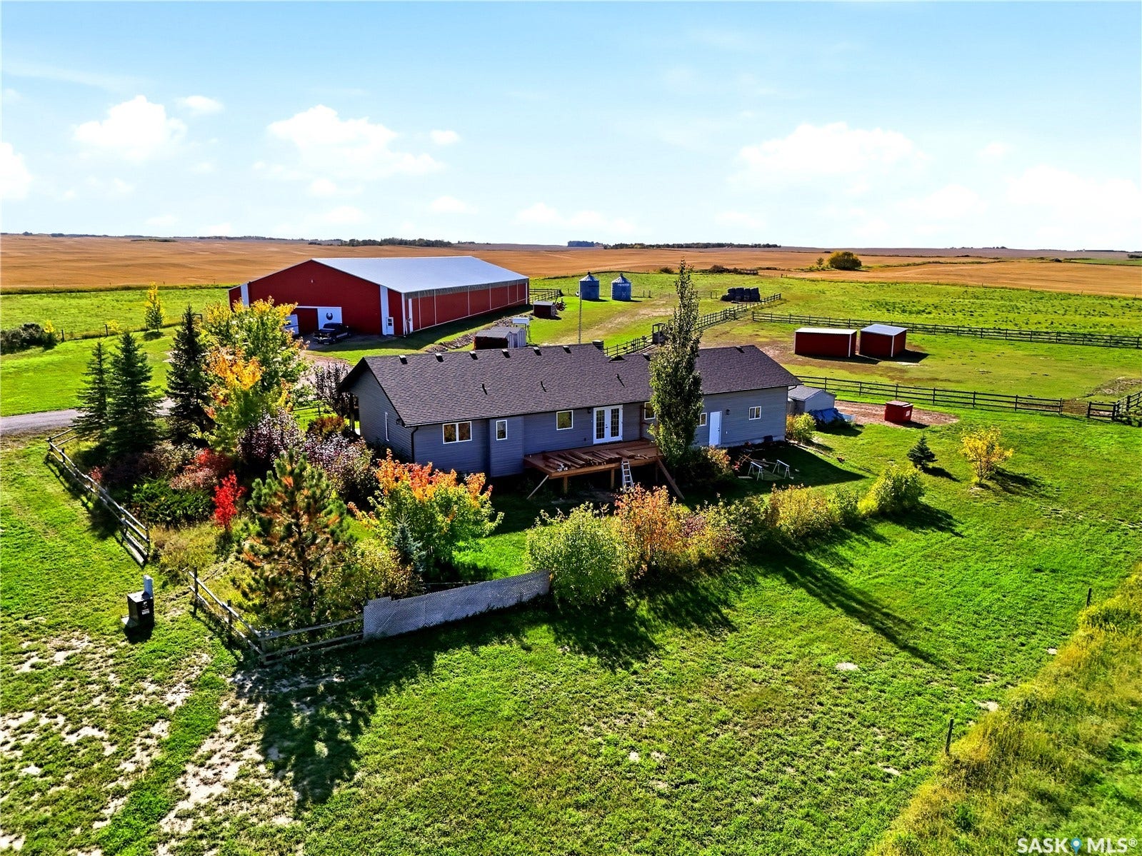 Expansive acreage featuring a single-story residence with a dark shingle roof, a large red barn with a metal roof, several outbuildings, and mature trees