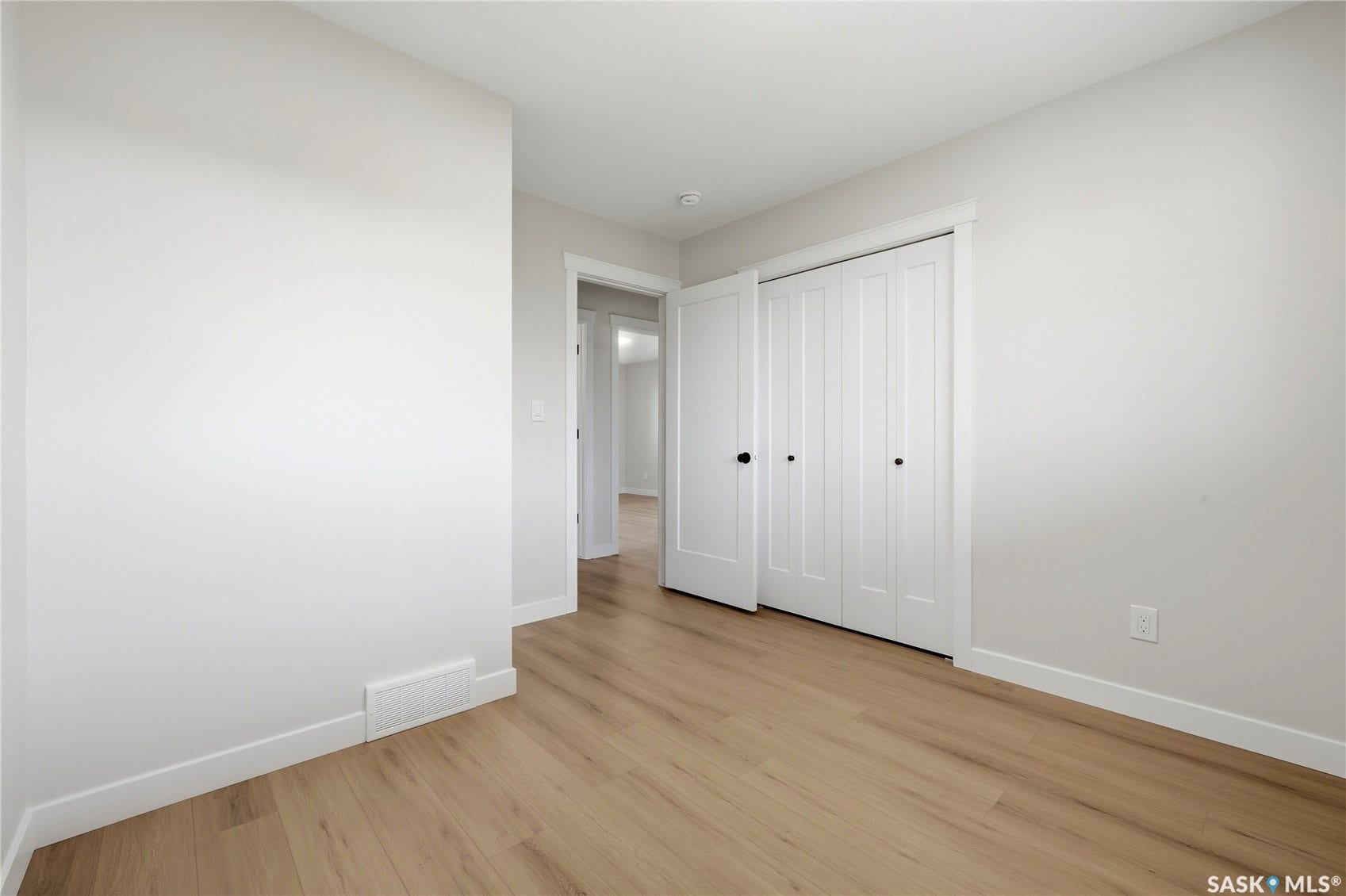 Light wood-finish flooring, white walls, white trim, and white bi-fold closet doors