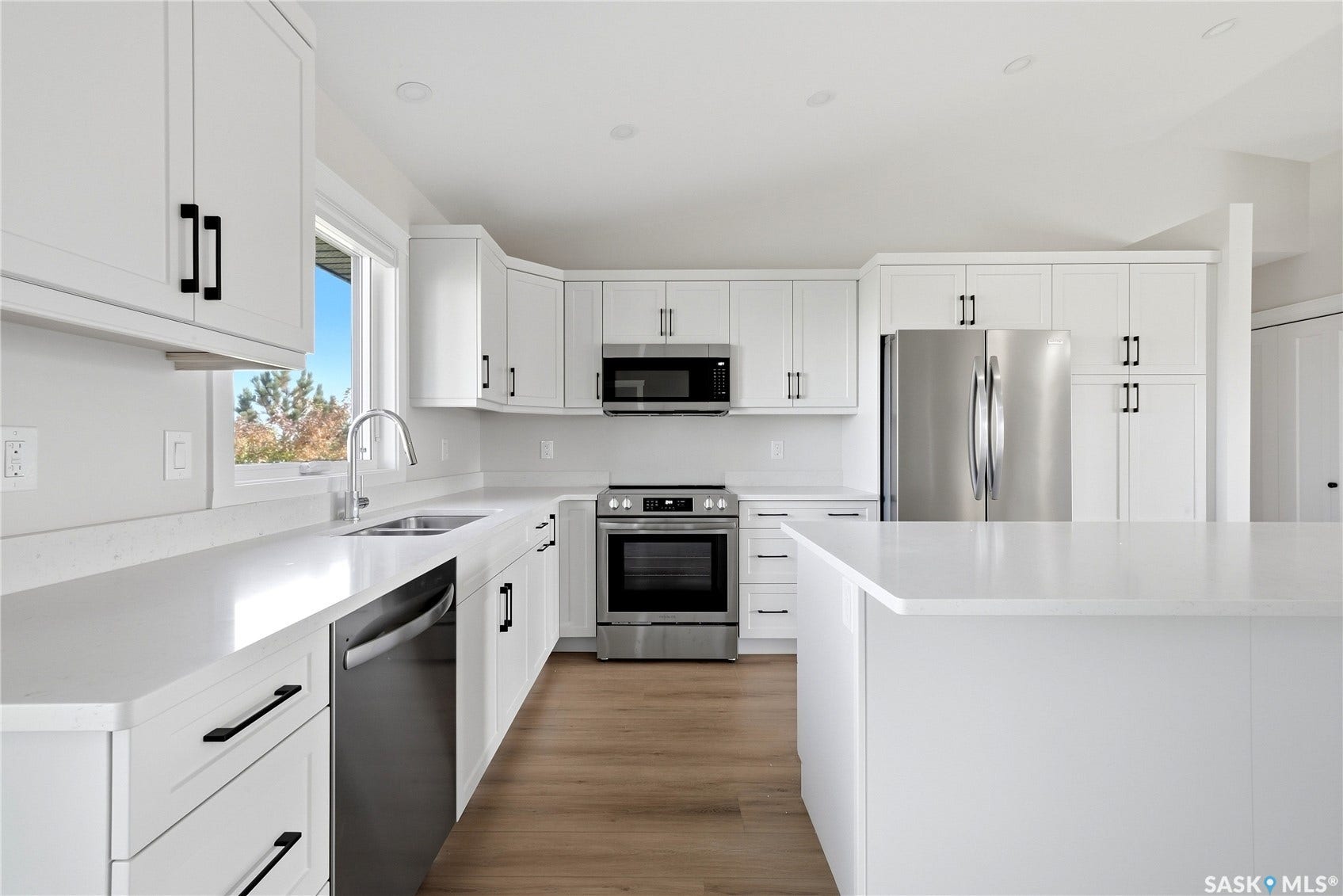 White cabinetry with black hardware, stainless steel appliances, light-toned countertops, wood-finish flooring, and recessed lighting