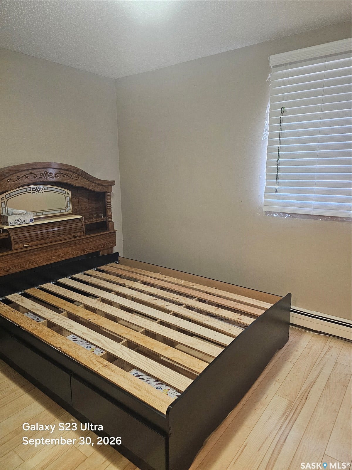 Wood-finish flooring with a window featuring horizontal blinds
