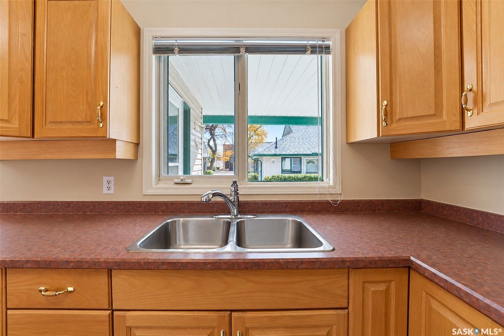 Kitchen featuring light wood cabinetry, double basin stainless steel sink, chrome faucet, and expansive countertop space