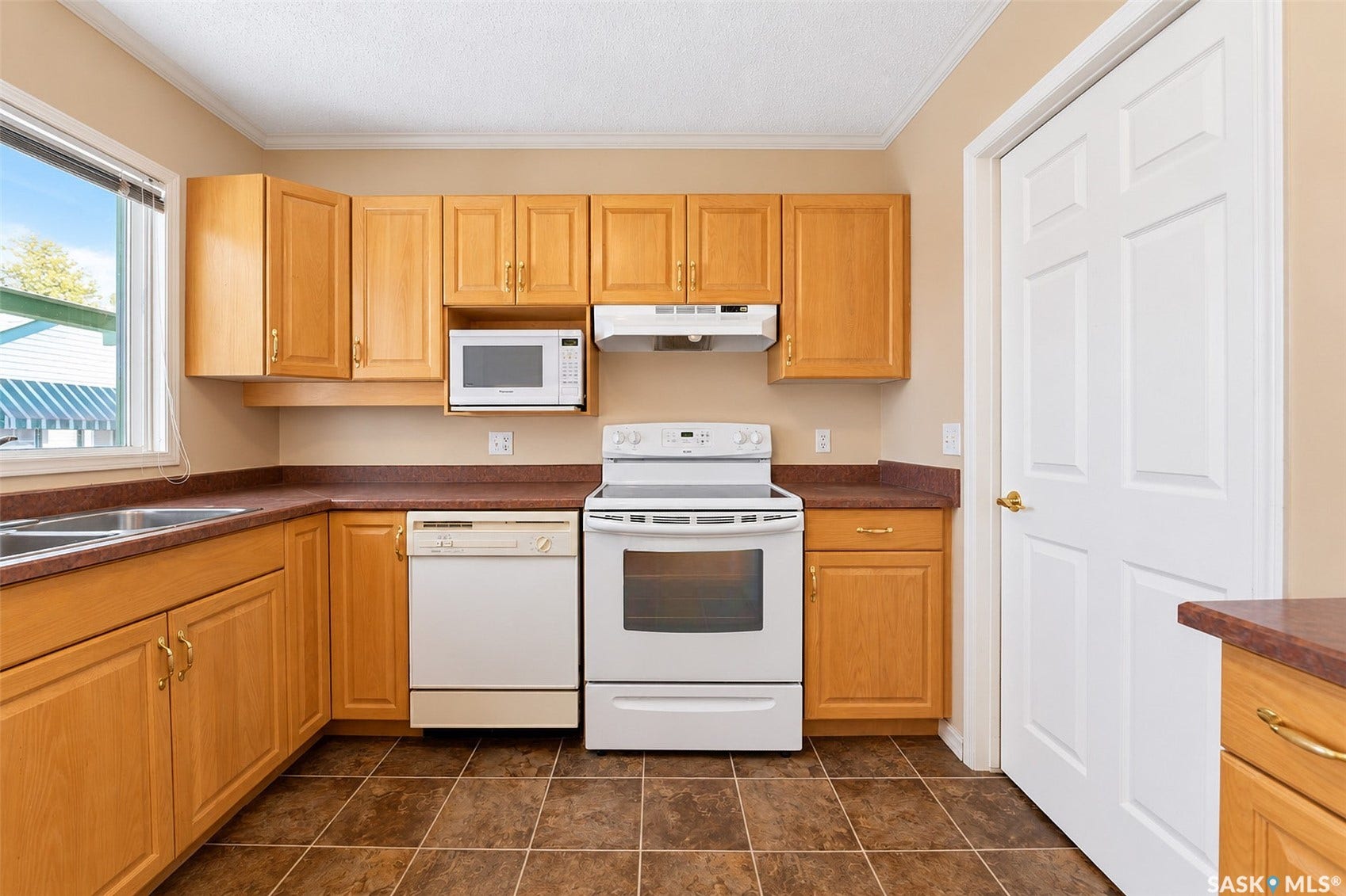 Wood-finish cabinetry with brass hardware, dual basin stainless steel sink, built-in microwave, white electric range, and tiled flooring