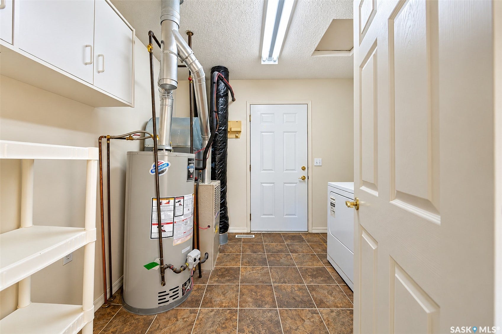 Utility area featuring square tile flooring, overhead storage cabinetry, and a service door
