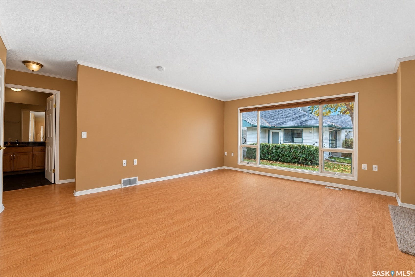 Expansive room featuring wood-finish flooring, a large picture window, crown molding, and a visible doorway to a bathroom with a vanity