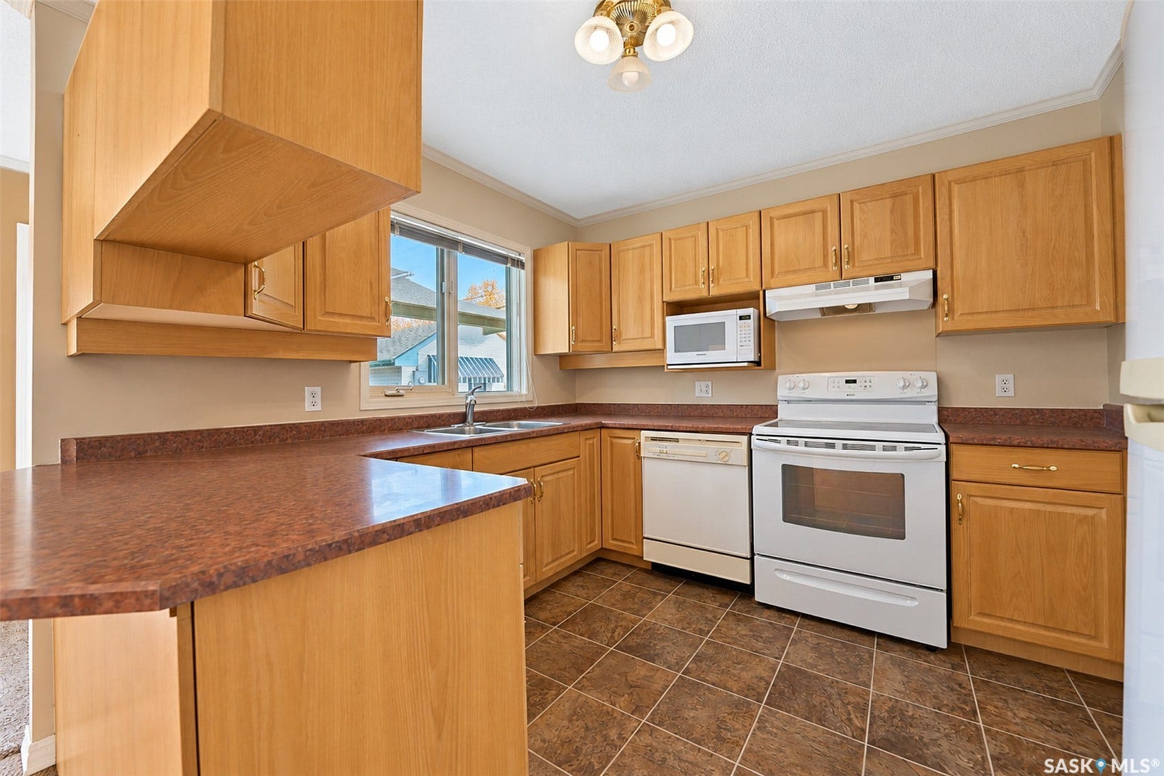 Kitchen featuring wood-finish cabinetry, integrated white appliances, L-shaped countertop, stainless steel sink, and tiled flooring