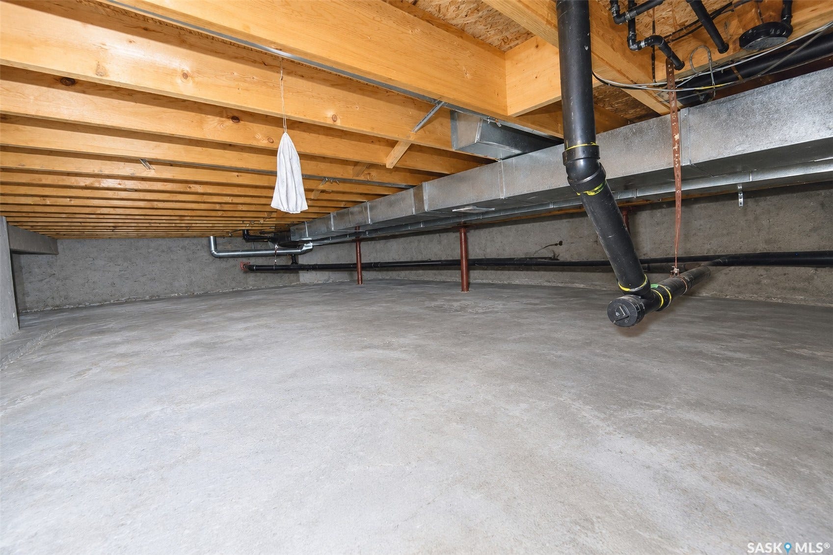 Unfinished space featuring exposed wood joists, concrete flooring, concrete block walls, and visible utility piping