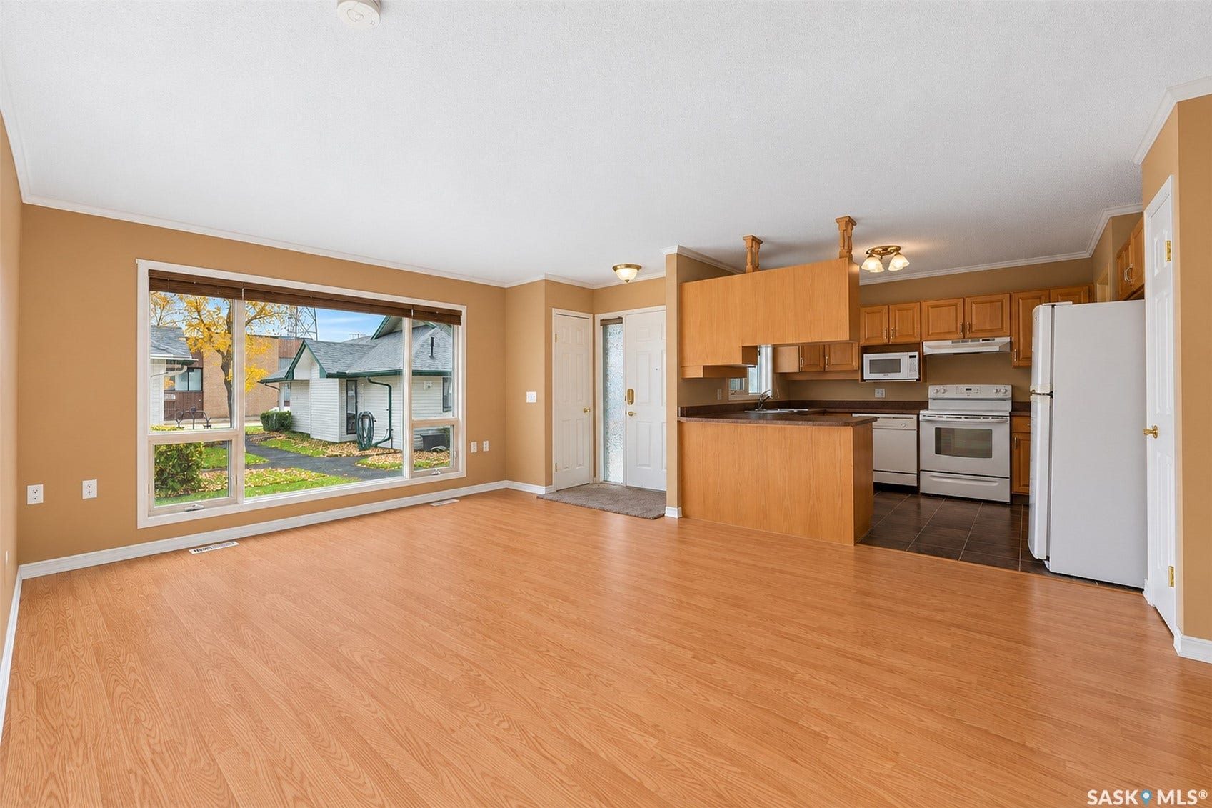 Wood-finish flooring, large picture window, kitchen with light wood cabinetry, stainless steel appliances, and a breakfast bar
