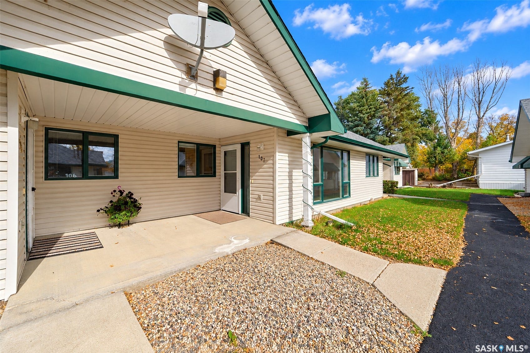 White siding exterior with green trim, covered concrete porch, concrete walkway, and gravel landscaping