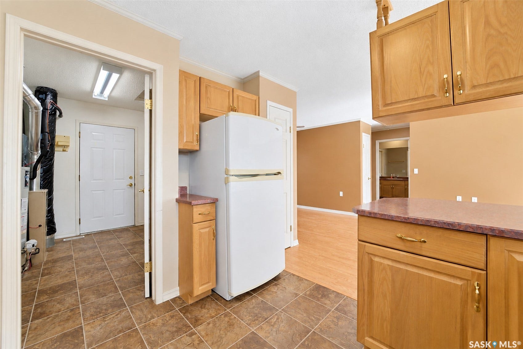 Wood-finish cabinetry with gold-tone hardware, a white two-door refrigerator, and a tiled utility area