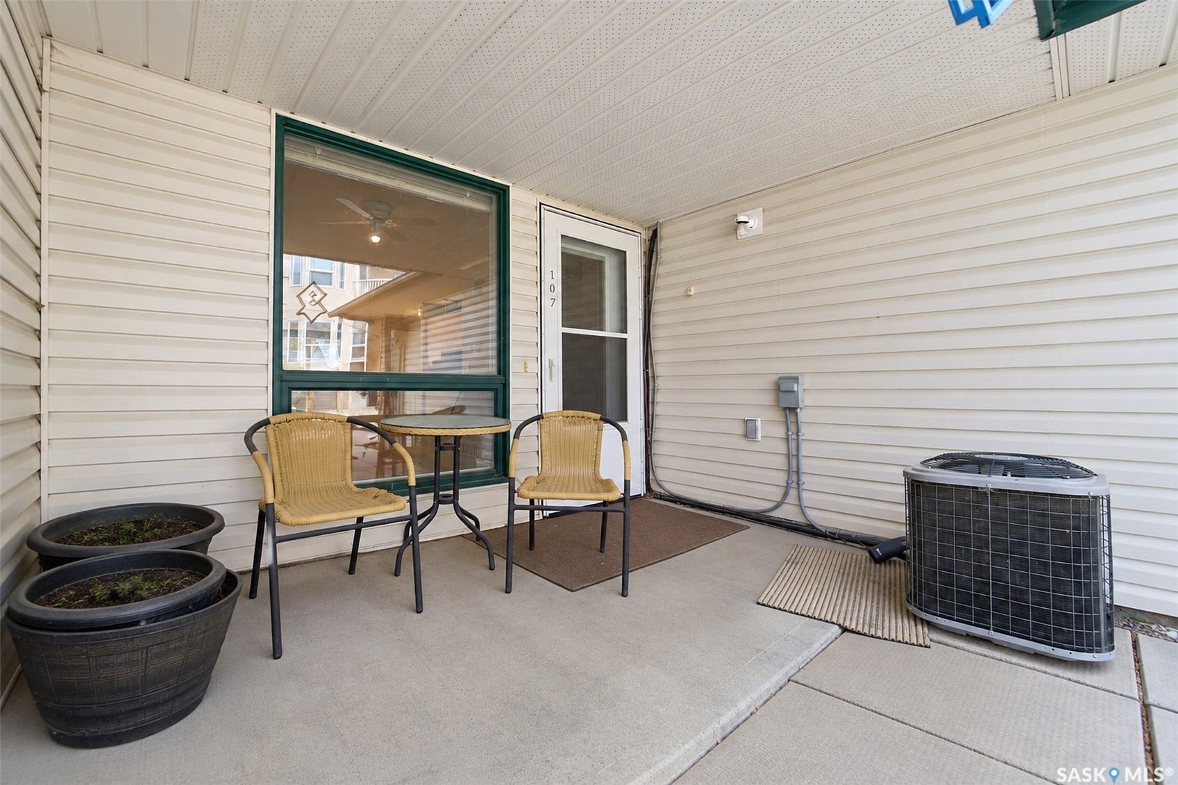 Covered concrete patio with white vinyl siding, a green-trimmed window, and a white exterior door