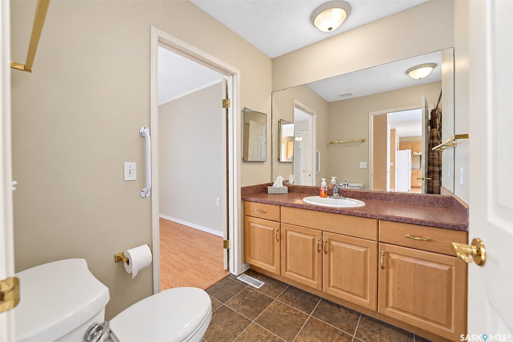 Vanity with integrated sink, extensive counter space, wood-finish cabinetry, and a large wall-mounted mirror