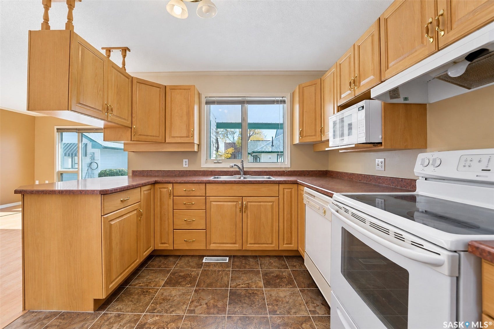 Kitchen featuring wood-finish cabinetry, a double basin sink, white range, white dishwasher, and an over-the-range microwave