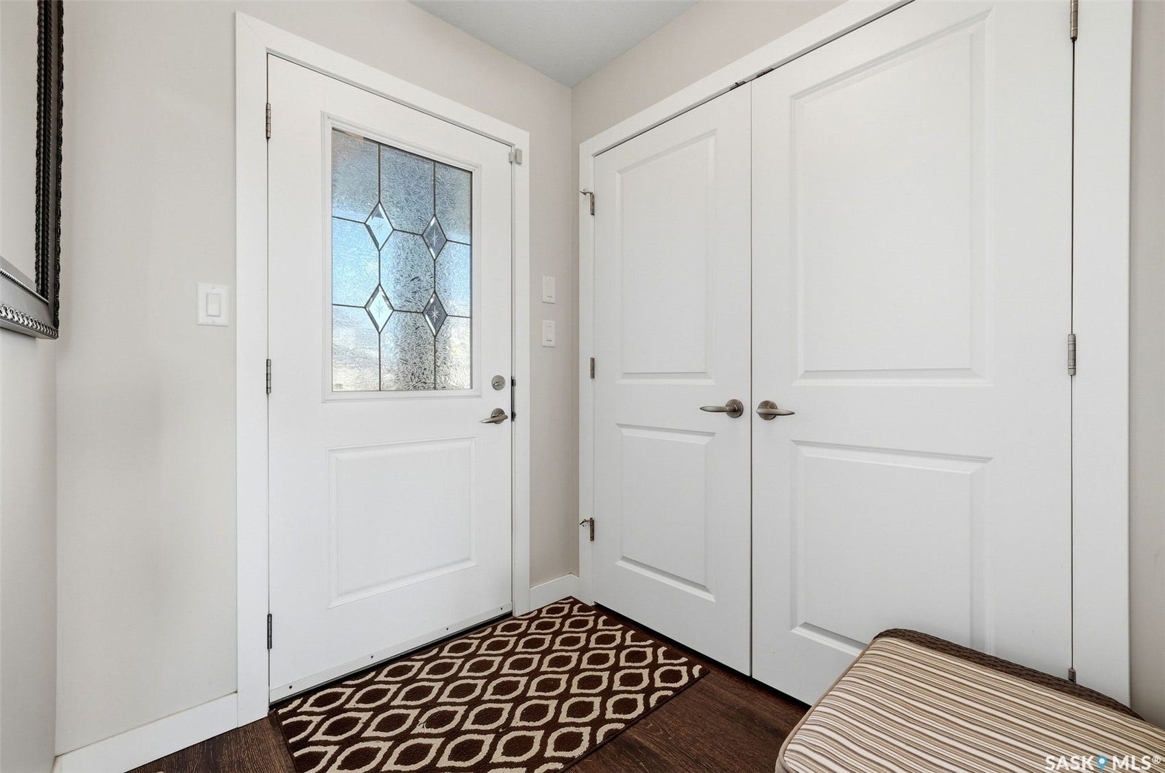 Entryway featuring wood-finish flooring, a white paneled door with decorative glass, and white bi-fold closet doors with brushed nickel hardware