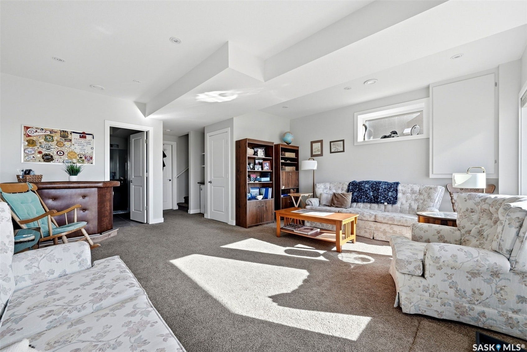 Recessed lighting, wood-finish built-in bar, wood-finish shelving unit, neutral carpet flooring, and a horizontal window