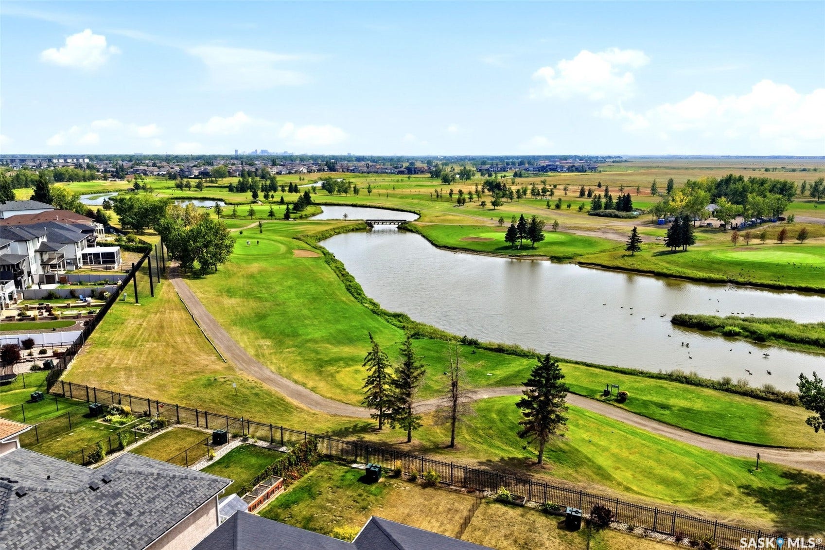 Expansive golf course frontage with a winding lake, established green spaces, and a distant city skyline