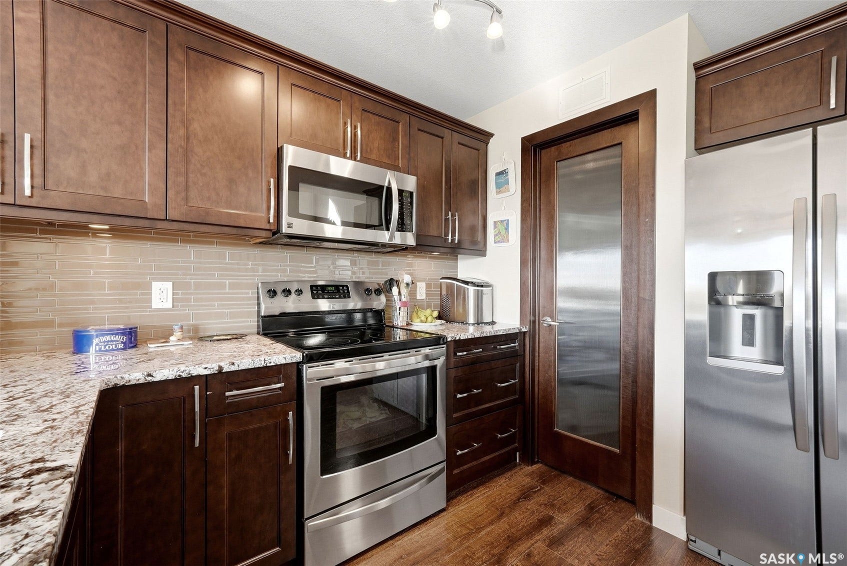 Dark wood-finish cabinetry, stainless steel appliances, granite countertops, tile backsplash, and wood-finish flooring