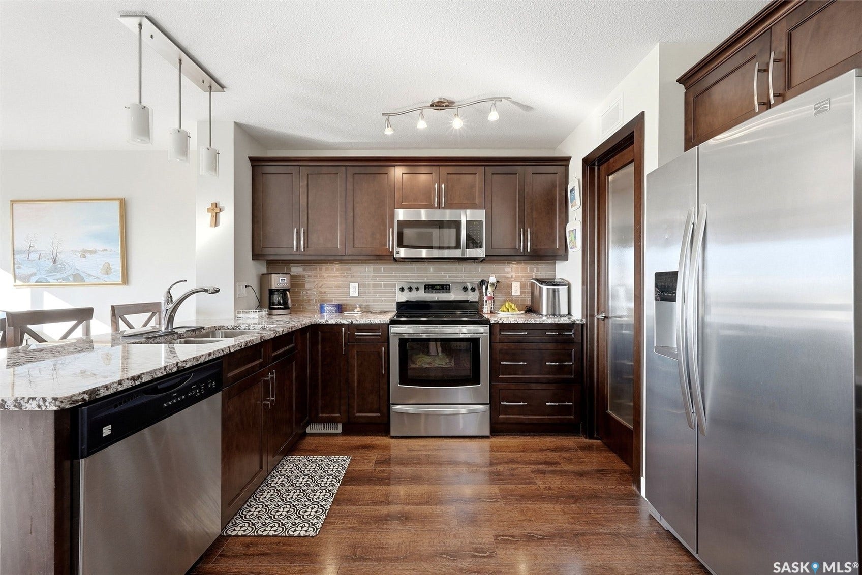 Kitchen featuring wood-finish flooring, dark wood cabinetry, stainless steel appliances, and a light-toned countertop