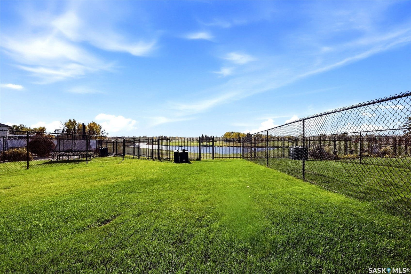 Expansive green lawn, black chain-link fencing, and a tranquil body of water