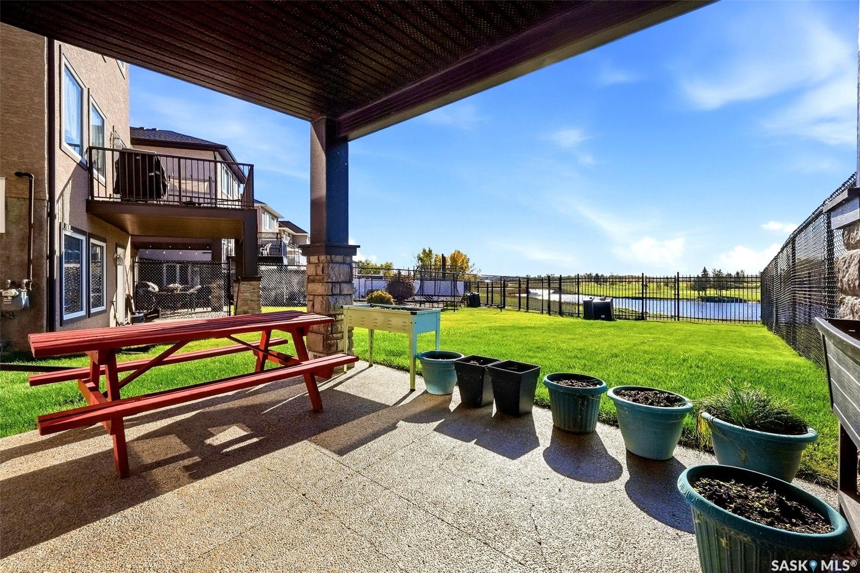 Expansive rear patio with overhead coverage, stone-clad pillar, manicured lawn, and black perimeter fencing