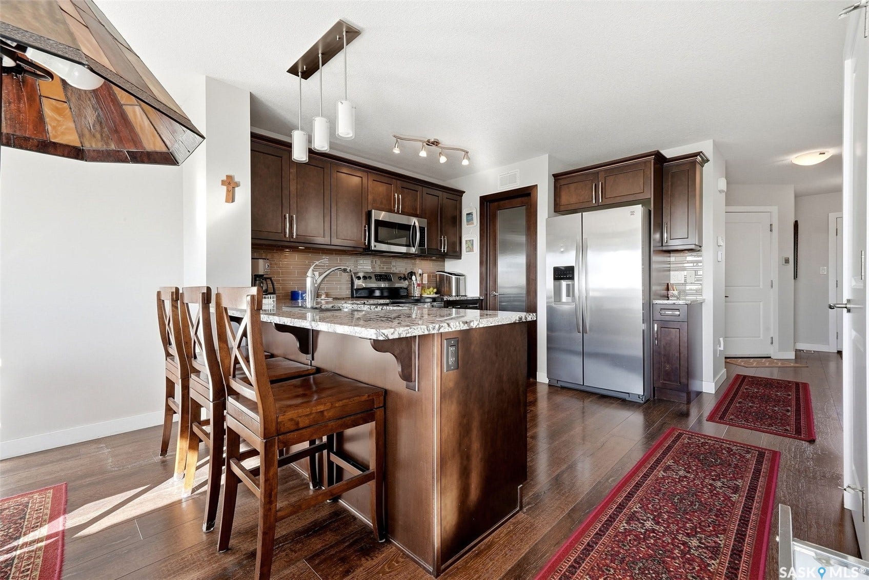 Kitchen with wood-finish flooring, dark wood cabinetry, stainless steel appliances, and a central island with a light-toned countertop