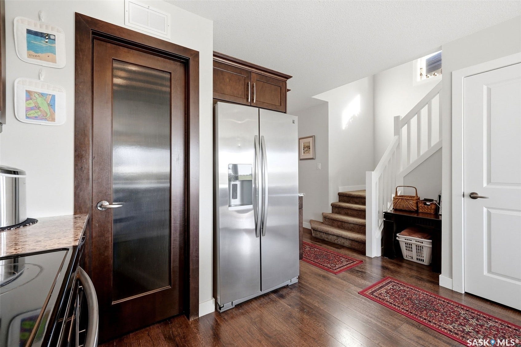 Stainless steel refrigerator, wood-finish flooring, dark wood cabinetry, and a staircase with white risers