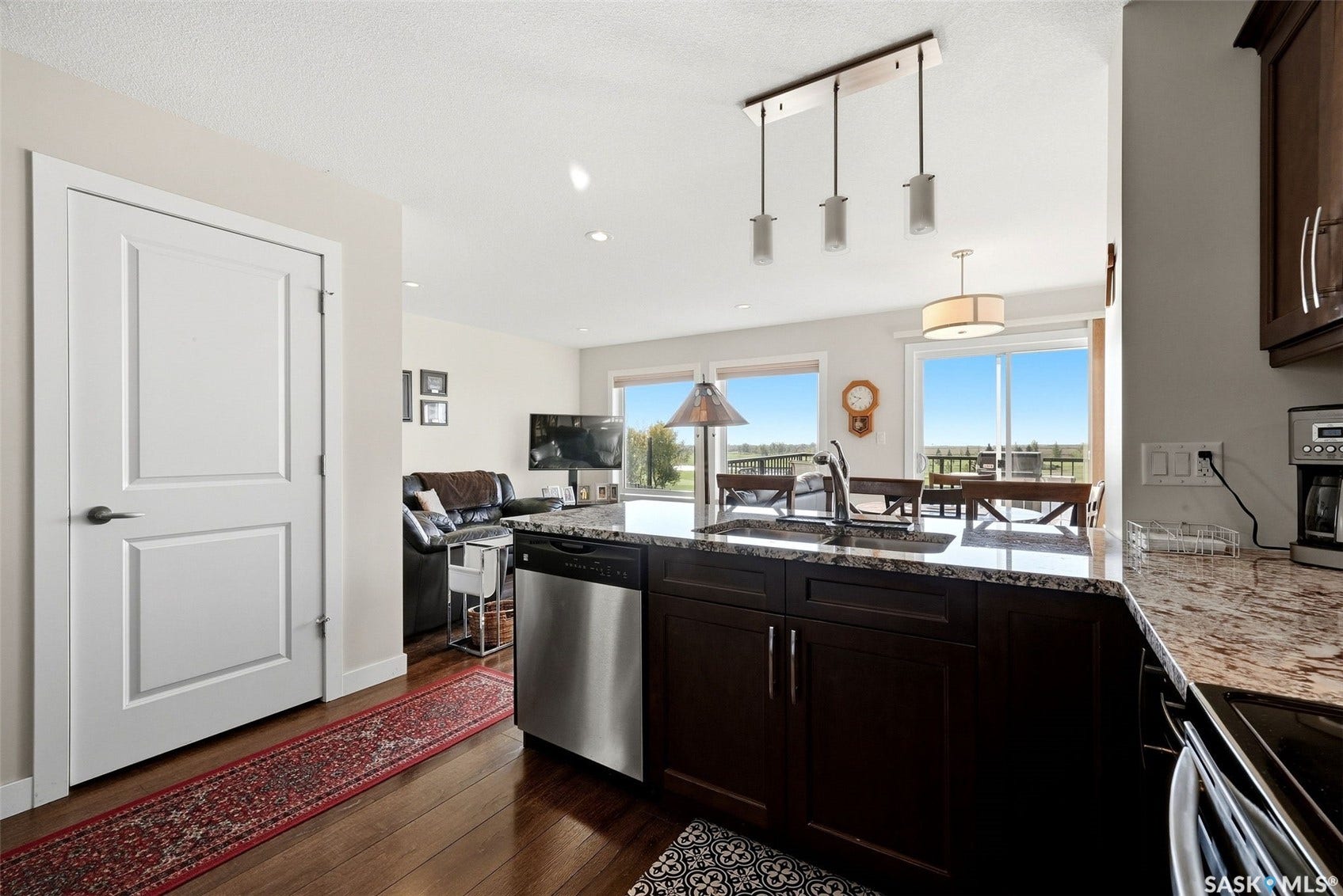 Kitchen island featuring granite countertops, stainless steel dishwasher, dark wood cabinetry, and an undermount sink