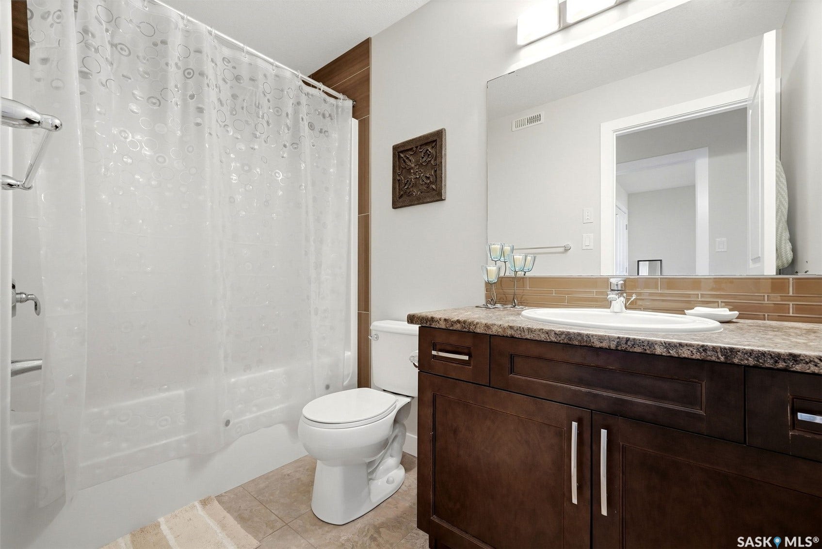 Bathroom featuring a dark wood-finish vanity, integrated sink, large mirror, and full bathtub with shower
