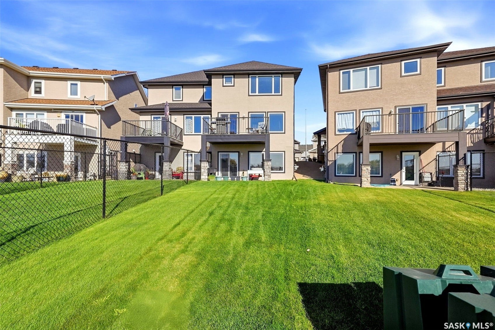 Stucco exterior with multiple windows, upper-level deck, lower-level patio, and a grassy lawn