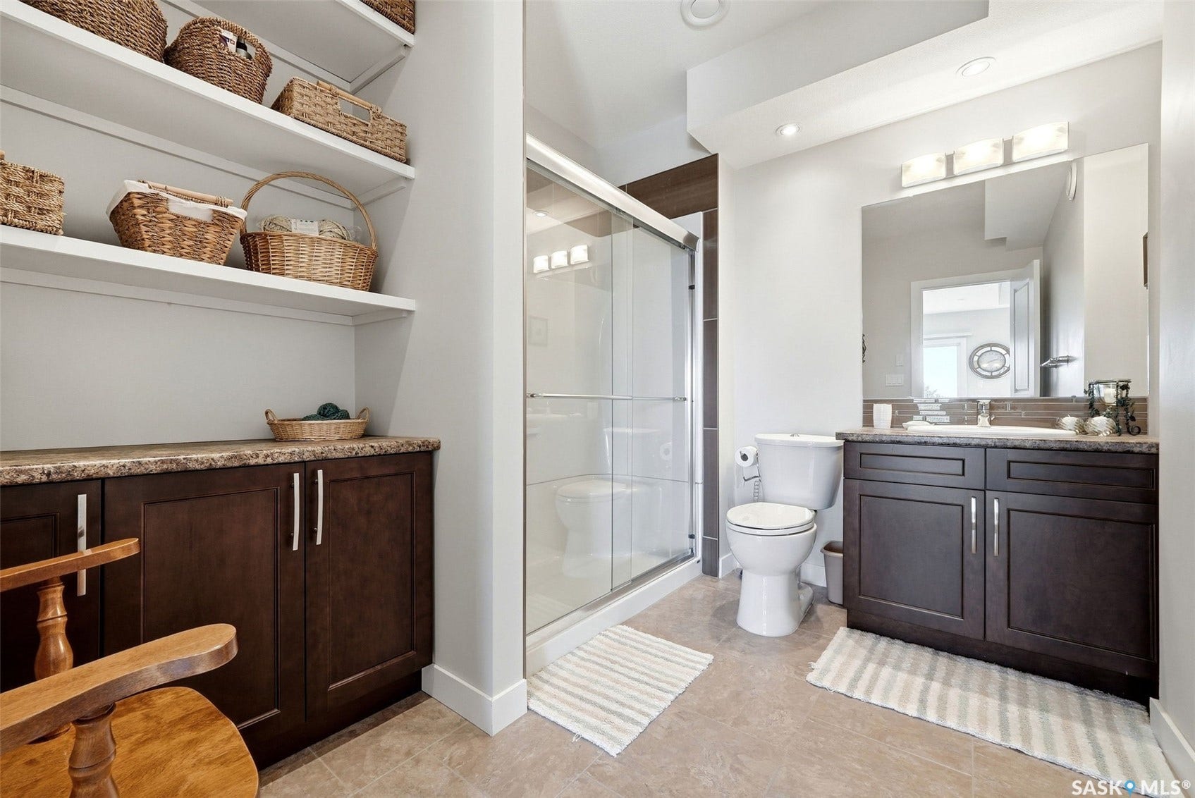 Walk-in shower with clear glass enclosure, a vanity with dark wood-finish cabinetry, a large mirror, and ample open shelving