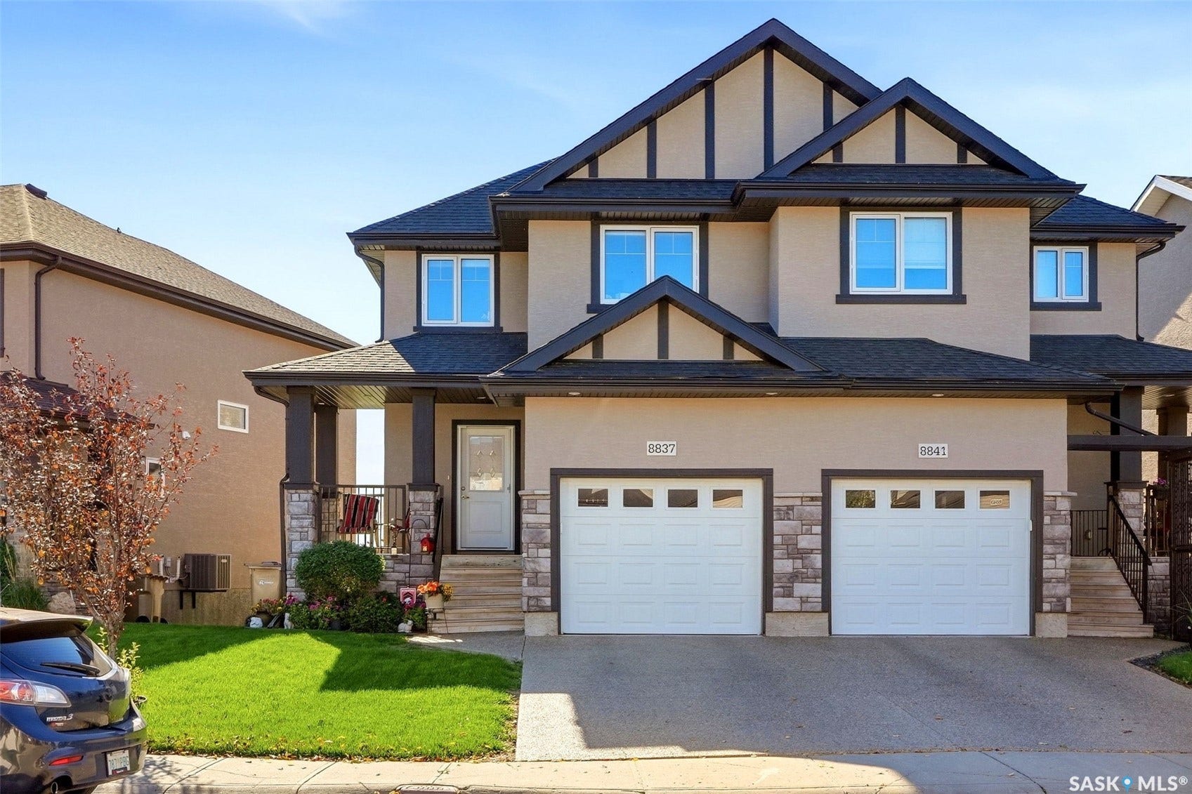 Stucco exterior with stone accents, architectural shingle roof, attached garages, and a covered porch entry