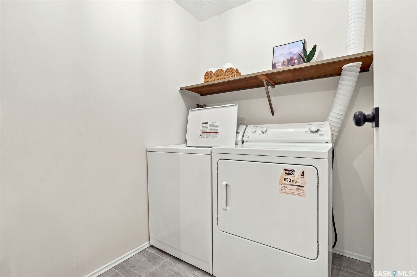 White washer and dryer units, wood-finish floating shelf, and neutral wall paint