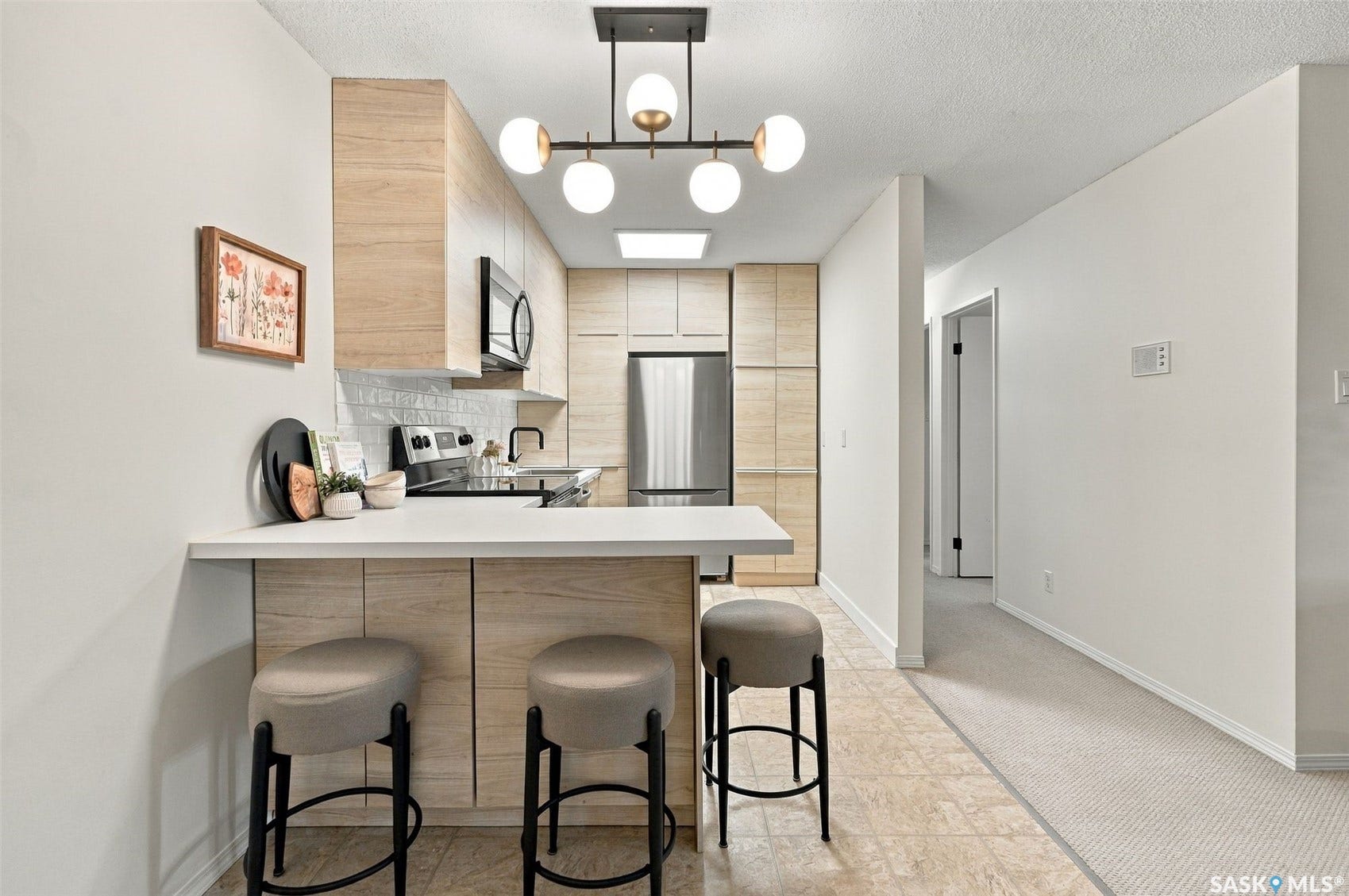 Kitchen featuring wood-finish cabinetry, stainless steel appliances, a white tile backsplash, and a contemporary linear chandelier