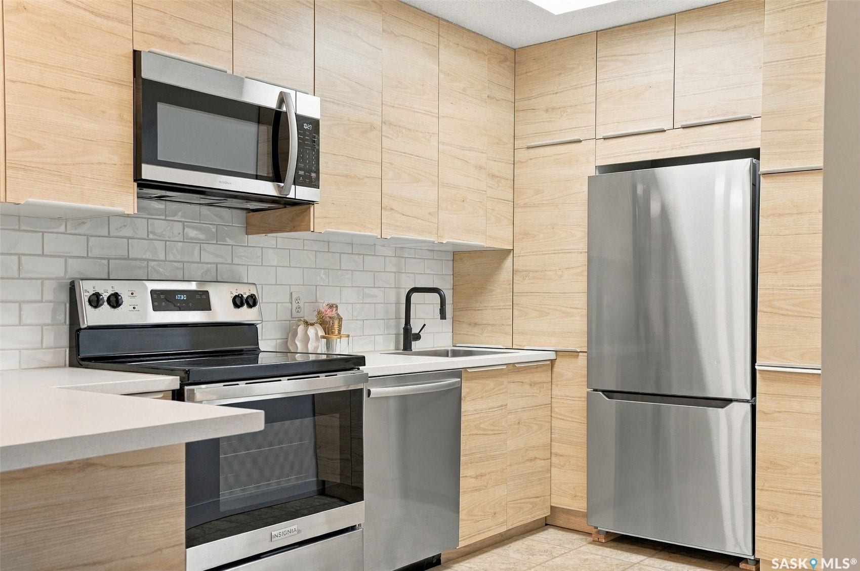 Contemporary kitchen featuring light wood-finish cabinetry, stainless steel appliances, white subway tile backsplash, and light-colored countertops