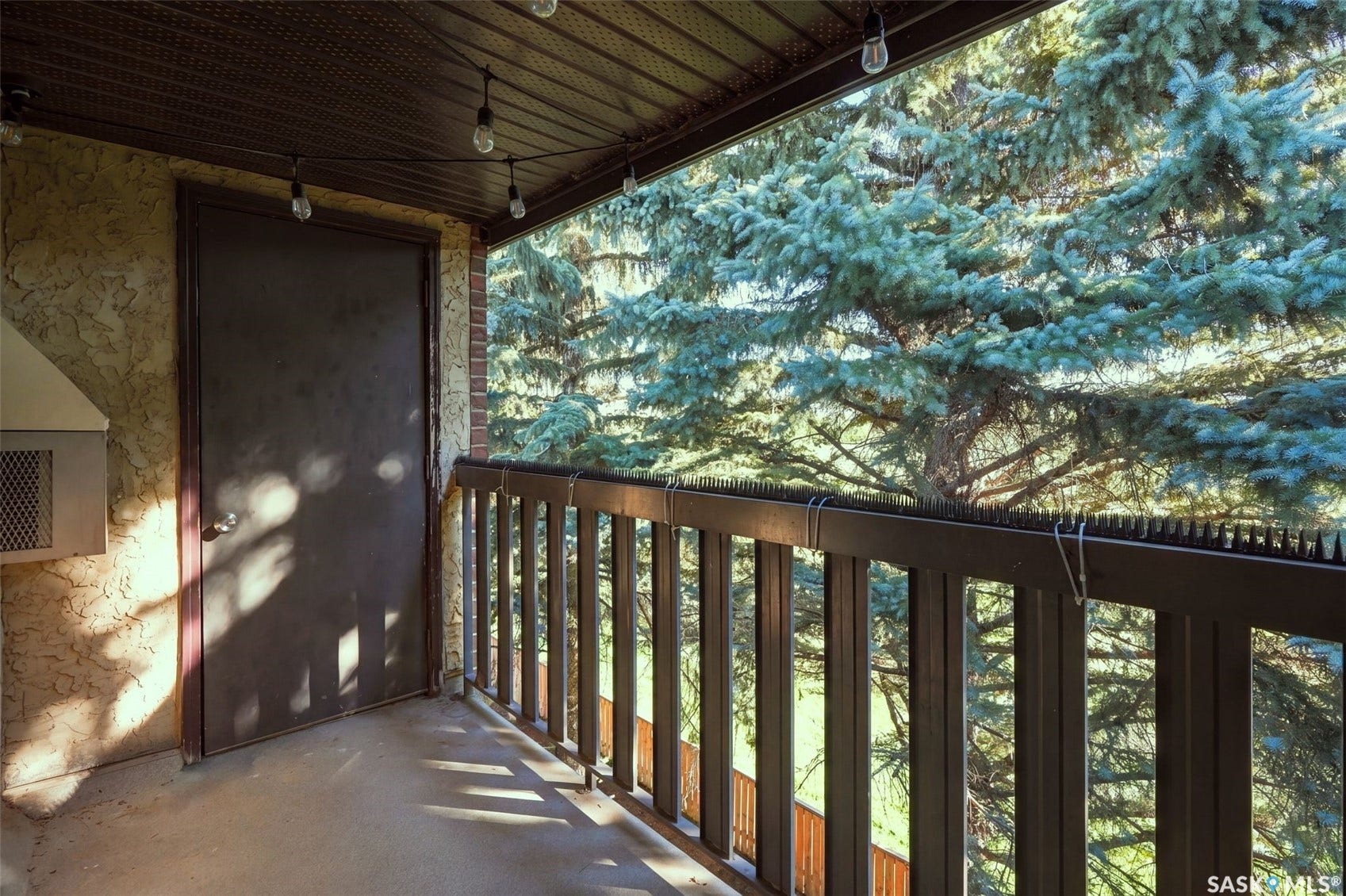 Outdoor balcony featuring a wood-finish railing, stucco exterior, and string lighting