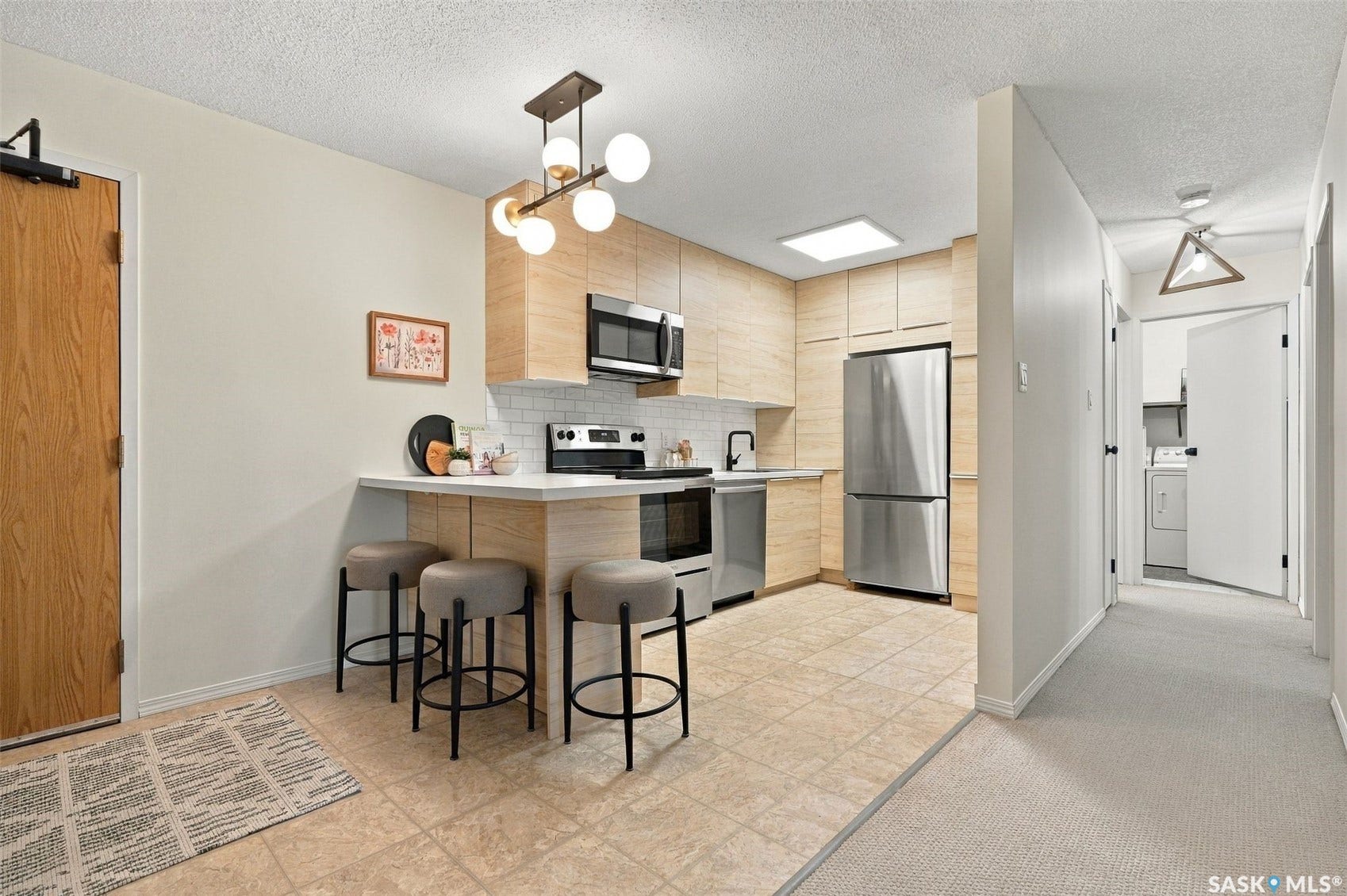 Functional kitchen featuring light wood-finish cabinetry, stainless steel appliances, white subway tile backsplash, and a breakfast bar with seating