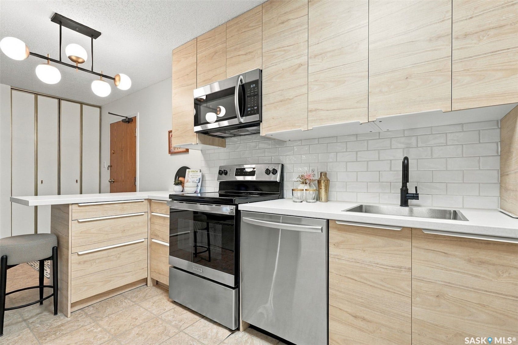 Light wood-finish cabinetry with integrated pulls, stainless steel appliances, white subway tile backsplash, white countertops, and a black-finish faucet