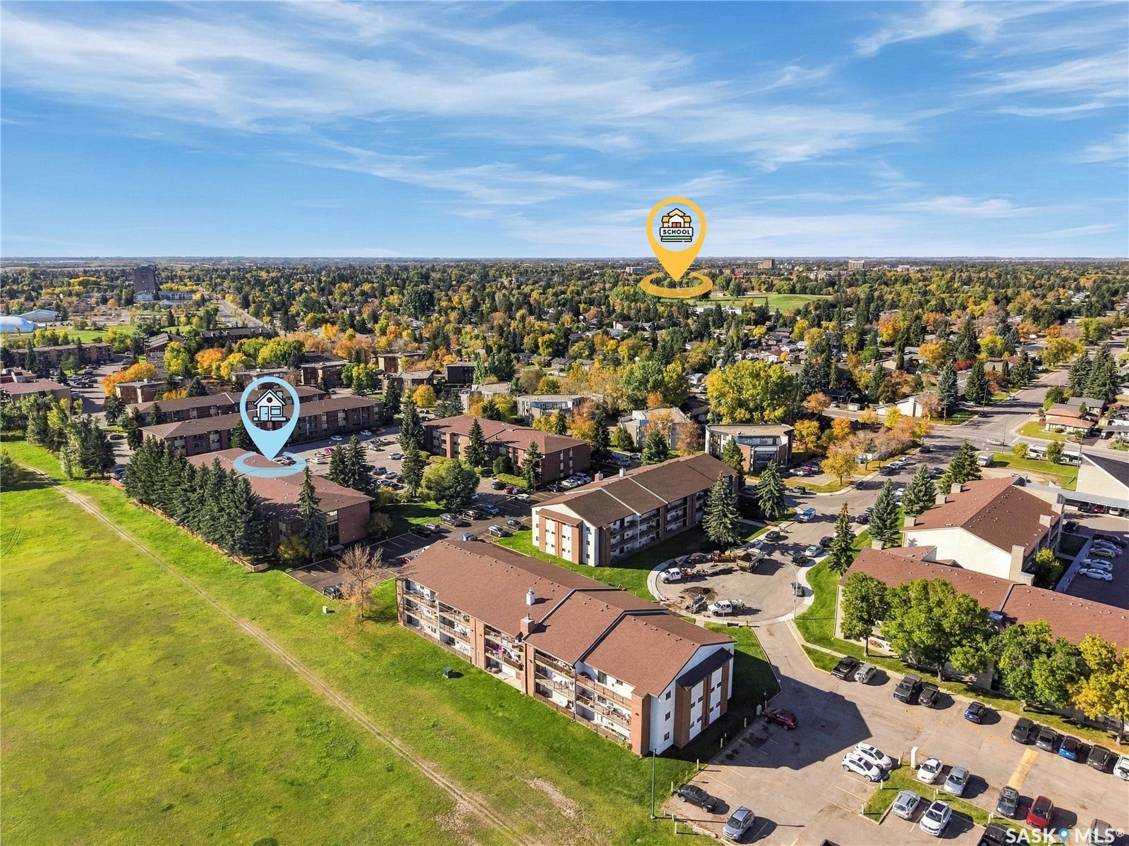 Expansive aerial perspective featuring multiple residential buildings with brown roofs, mature trees, and paved parking areas