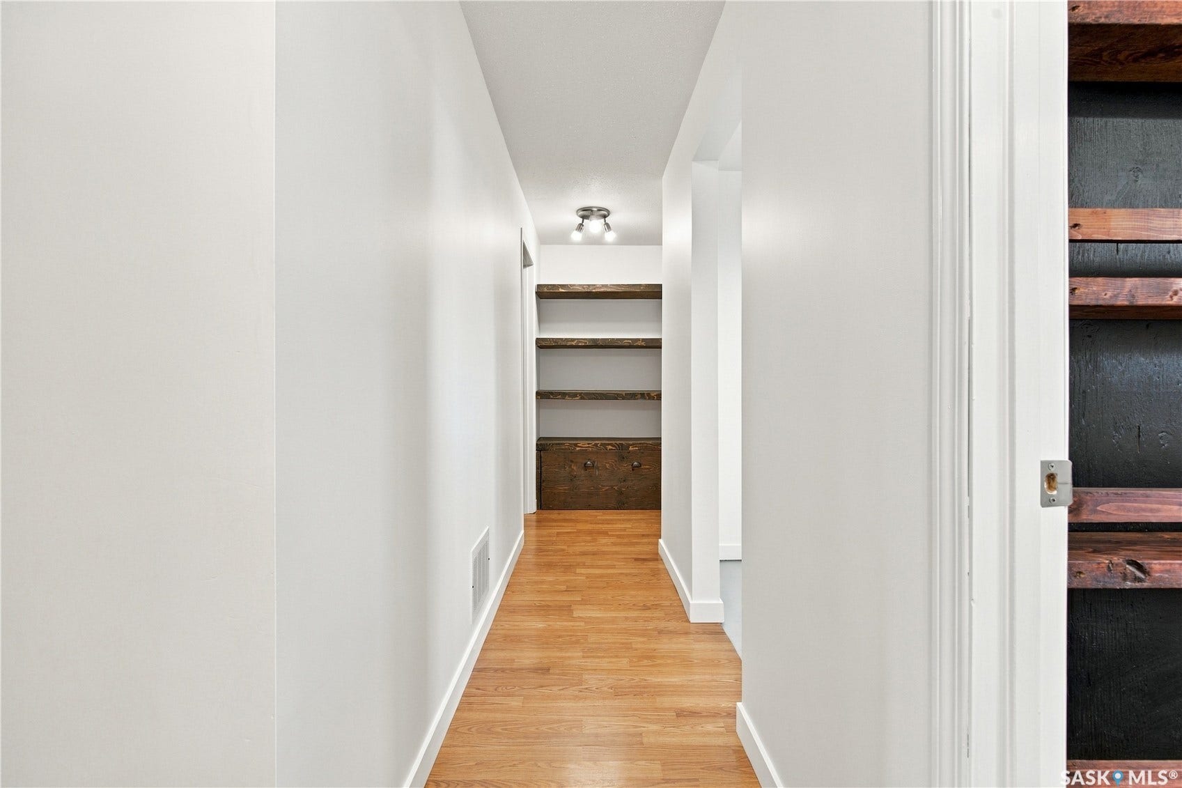 Hallway featuring wood-finish flooring, white walls, and built-in shelving with a dark accent wall