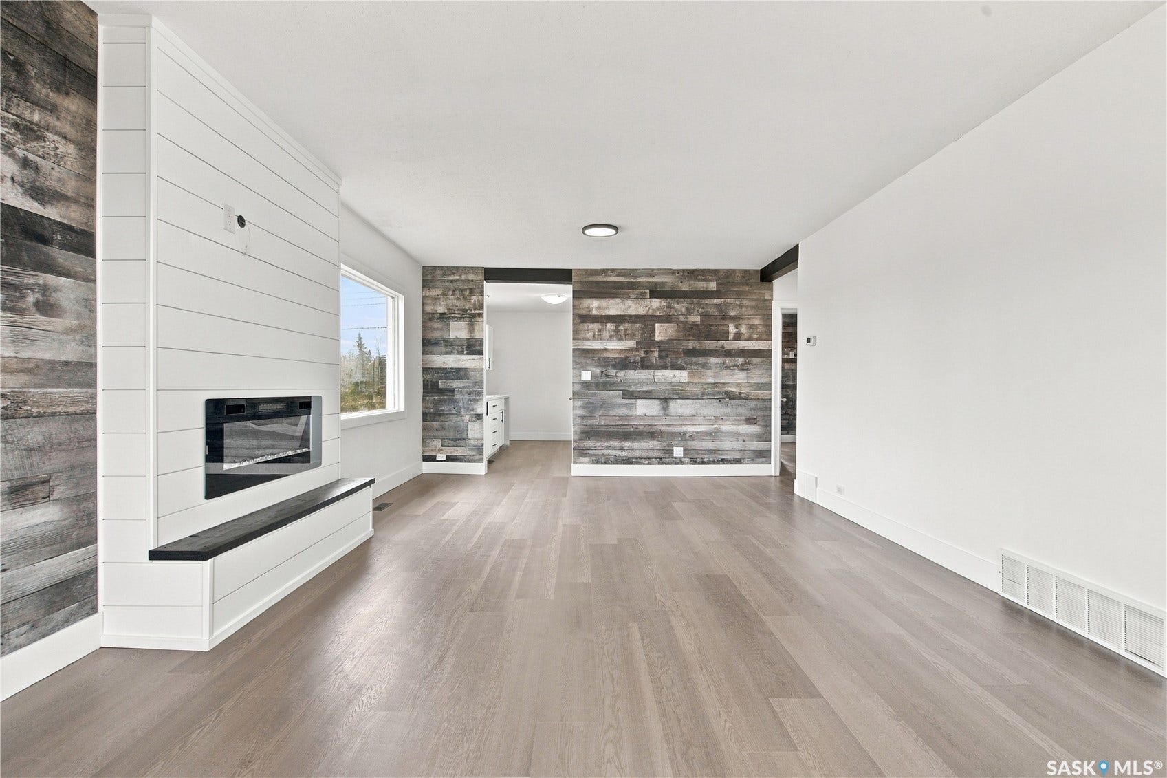 Wood-finish flooring, integrated linear fireplace with white shiplap surround, built-in hearth with black top, recessed ceiling light, and accent wall with wood paneling