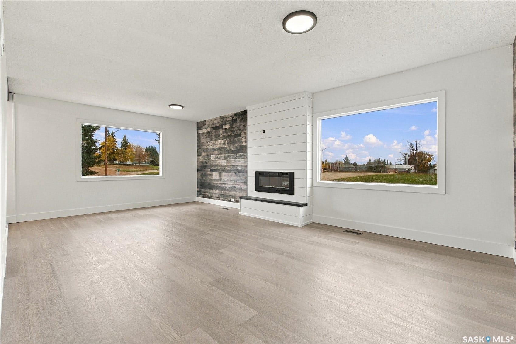 Spacious room featuring light wood-finish flooring, a contemporary fireplace with a shiplap surround, and accent wall with dark wood-finish paneling